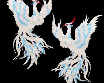 Puede incluir: Dos fénix bordados blancos con detalles azules y rojos. Los fénix están mirando en direcciones opuestas y tienen colas largas y fluidas.