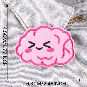 May include: Pink felt iron-on patch of a cartoon brain with a smiling face. The patch is 1.77 inches tall and 2.48 inches wide.