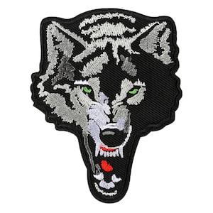 May include: Embroidered iron-on patch featuring a snarling wolf's head with green eyes and a red mouth. The wolf is depicted on a black background with gray and white fur details.