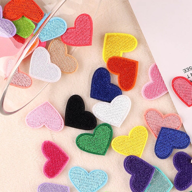 May include: Assortment of colorful felt heart patches in various colors, including red, pink, blue, green, yellow, black, and white. The patches are in a variety of sizes and shapes, and some have a glittery finish.