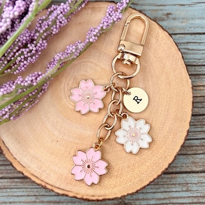 May include: Gold keychain with three pink and white cherry blossom charms and a gold charm with the letter R.