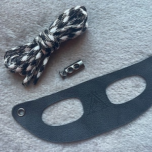 May include: Black and white striped shoelace, a silver metal toggle, and a black leather mask with two eye holes.