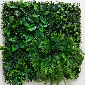 Puede incluir: Un panel de pared de plantas artificiales cuadrado con un arreglo denso de varios follajes verdes, incluyendo hojas anchas, frondas tipo palma y ramitas delicadas similares a helechos, en múltiples tonos de verde.
