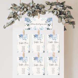 May include: A set of six blue and white floral wedding table cards with the text "Please find your seat" at the top. Each card has a table number and a list of names.