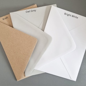 K&ouml;nnte beinhalten: Eine Auswahl an Umschl&auml;gen in den Farben Kraft, Eulen-Grau und Hellwei&szlig;. Die Umschl&auml;ge sind geschichtet und zeigen ihre verschiedenen Farbt&ouml;ne und Texturen. Die Farbbezeichnungen sind aufgedruckt.