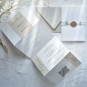 K&ouml;nnte beinhalten: Elegante Hochzeitseinladungssuite in Wei&szlig;- und Beiget&ouml;nen. Die gefaltete Einladung zeigt den Text &bdquo;The wedding of Rebecca and Jonathan&ldquo; und enth&auml;lt Details, RSVP und einen QR-Code. Ein passender Umschlag und eine versiegelte Einladung sind ebenfalls enthalten.