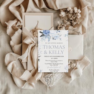 May include: A wedding invitation with a blue floral design. The invitation reads "We are getting married, Thomas & Kelly, Friday 16th November 2024 at 1:30pm. Please arrive for 1pm for our ceremony to begin at 1:30pm. Grand Palladium Hall, Beechgrand Hotel, Essex, CB10 1XB. Reception to follow at The Barn at Mew Farm, Essex, CB11 2XB."