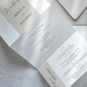 K&ouml;nnte beinhalten: Eine dreifach gefaltete Hochzeitseinladung in neutralen Farbt&ouml;nen mit den Namen "Rebecca und Jonathan" in eleganter Schrift. Die Einladung enth&auml;lt Details zur Zeremonie, wie Datum, Uhrzeit und Ort.