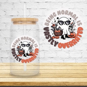 May include: A clear glass tumbler with a bamboo lid and a straw. The tumbler has a sticker on it that says "Being normal is vastly overrated" with a cartoon ghost wearing sunglasses and holding a pumpkin.