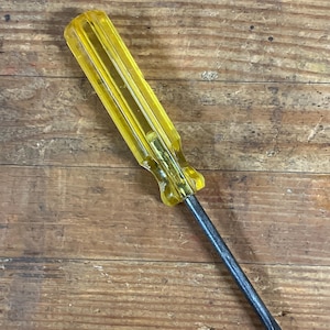 May include: A flathead screwdriver with a clear yellow handle and a silver metal shaft. The handle is ribbed for grip and the blade is flat. The tool is designed for turning screws.