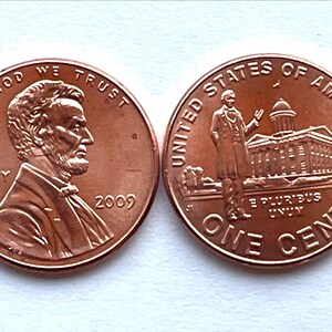 May include: Two copper-colored United States one-cent coins. One coin features Abraham Lincoln's profile and the word "LIBERTY" with the year 2009. The other coin shows the Lincoln Memorial and the words "ONE CENT". The words "IN GOD WE TRUST" and "UNITED STATES OF AMERICA" are also visible.