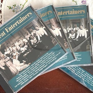 May include: Four compact discs with a teal background and gold lettering. The discs are titled "The Great Entertainers" and feature a variety of musical artists, including Doris Day, Judy Garland, Louis Armstrong, and Cab Calloway.