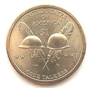 May include: A gold-colored $1 coin featuring two military helmets, crossed feathers, and the text "UNITED STATES OF AMERICA." The coin also includes the text "WWI," "WWII," and "CODE TALKERS."