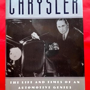 May include: Book cover with the title "CHRYSLER" in large, bold, blue letters. The cover features a black and white photograph of a man in a suit standing next to a vintage car. The text below reads "THE LIFE AND TIMES OF AN AUTOMOTIVE GENIUS" and "Vincent Curcio".