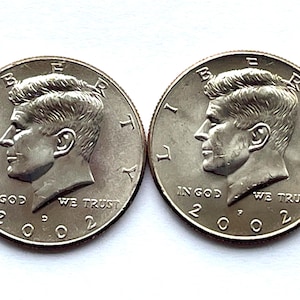 May include: Two silver Kennedy half-dollar coins. Each coin features a profile of John F. Kennedy, the words "IN GOD WE TRUST", and the year "2002". The coins are displayed on a white background.