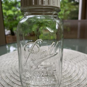 May include: A clear glass Ball brand jar with a white lid. The jar has a textured surface and the words "Ball" and "Perfect Mason" are printed on the front.