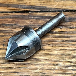 May include: A metal countersink drill bit with a conical tip and a cylindrical shank. The tool is silver-colored and has the text "U.S.A." stamped on its side. The drill bit is designed for creating countersunk holes.