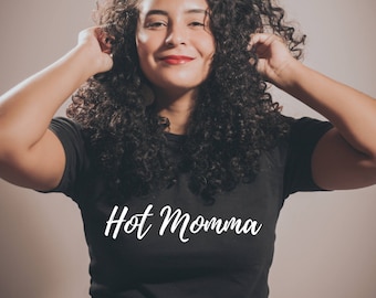 以下が含まれることがあります： 黒髪で巻き毛の女性が、「Hot Momma」という白い文字が書かれた黒いTシャツを着ています。