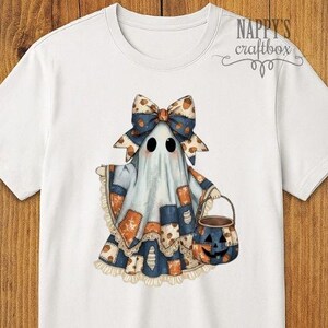 May include: White t-shirt featuring a cartoon ghost with a bow, patchwork outfit, and a pumpkin bucket. The ghost has black eyes and is wearing a blue and orange patchwork outfit. The text "Nappy's Craftbox" is in the upper right corner.