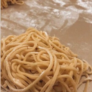 May include: A close-up of three piles of fresh, golden-brown noodles on a brown surface. The noodles are arranged in a loose, tangled pile, and they appear to be dusted with flour.