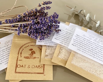 May include: Two small brown paper packets with white powder inside. The packets are labeled "Oat & Daisy Sourdough Starter" and have instructions for making sourdough starter. The packets are sitting on a light brown surface with a bouquet of dried lavender flowers.