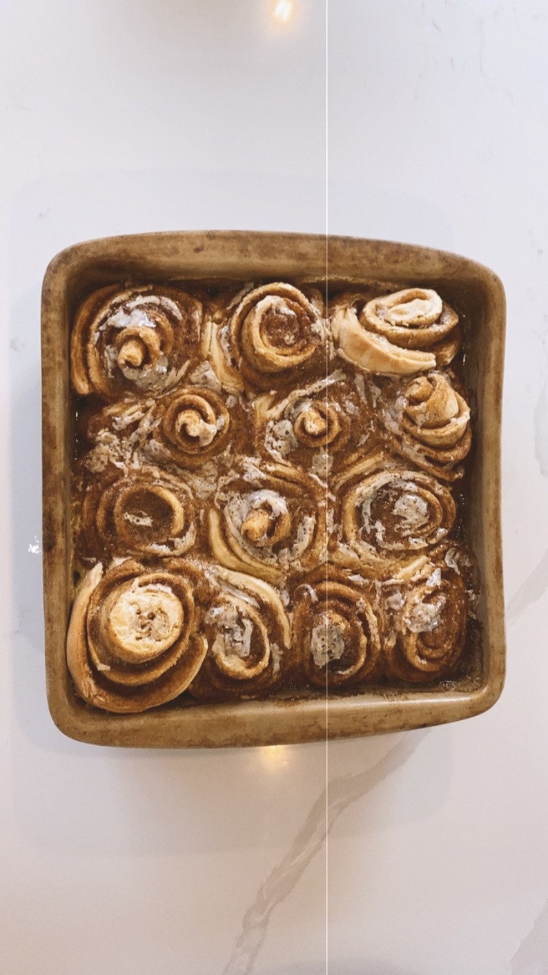 May include: A close-up of a baking dish filled with freshly baked cinnamon rolls, glazed with a sweet icing. The rolls are golden brown and have a swirl pattern.