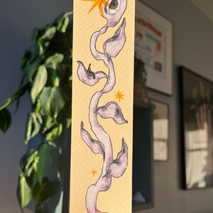 May include: A hand-drawn illustration of a stylized plant with a large eye at the top. The plant is drawn in shades of purple and gray on a yellow background. There are small yellow stars scattered around the plant.