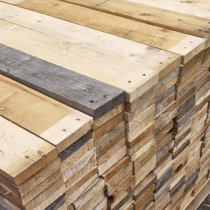 May include: A pile of reclaimed wooden planks in shades of brown and grey. The planks are stacked neatly, showcasing the natural grain and texture of the wood. The image highlights the rustic and weathered appearance of the wood, suitable for various projects.