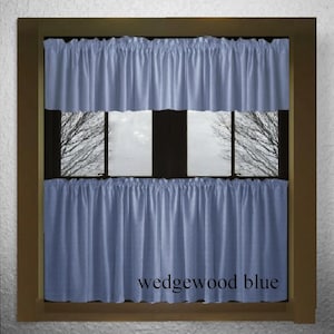 May include: A set of two blue valance curtains with a ruffled edge. The curtains are hung on a window with a wooden frame. The text "wedgewood blue" is printed on the bottom of the image.