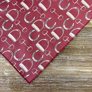 May include: A red fabric bandana with a white pattern of horseshoes and stirrups.