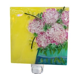 May include: A yellow glass night light with a pink flower bouquet in a blue vase. The night light has a white switch on the bottom.