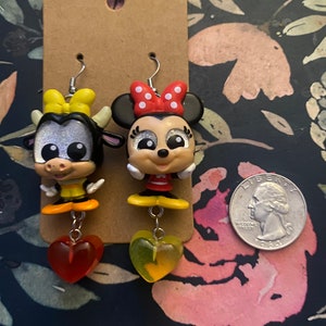 Peut inclure: Une paire de boucles d'oreilles pendantes avec une vache de dessin anim&eacute; et une souris de dessin anim&eacute; avec des pois rouges et blancs. Les boucles d'oreilles ont des breloques en forme de c&oelig;ur jaunes et rouges.