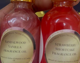 May include: Two glass fragrance oil bottles with gold caps and white droppers. One bottle is pink with "Sandalwood Vanilla Fragrance Oil" label. The other is red with "Strawberry Shortcake Fragrance Oil" label. Each bottle is 2 fl oz.