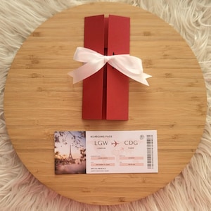 May include: A red invitation card tied with a white ribbon, placed on a wooden surface. A boarding pass with the text "LGW London" and "CDG Paris" is also present. The invitation card is a rectangular shape with a folded design.