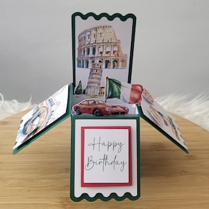 Può includere: Un biglietto di compleanno pop-up a tema italiano. La carta presenta illustrazioni del Colosseo, della Torre Pendente di Pisa e di un'auto sportiva rossa. Sono visibili anche una bandiera italiana e le parole "Happy Birthday".