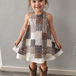 Könnte beinhalten: Ein ärmelloses Neckholder-Kleid mit einem Patchwork-Muster aus verschiedenen braunen, grauen und weißen Blumen- und geometrischen Drucken. Das Kleid hat einen einfarbigen weißen Saum und wird mit einer passenden Haarschleife und braunen Cowboystiefeln aus Leder kombiniert.