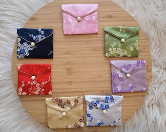 May include: Seven small fabric pouches with floral patterns and a button closure. The pouches are arranged in a circle on a wooden surface.