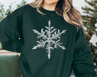 May include: A dark green sweatshirt with a white snowflake design. The snowflake is detailed and intricate.