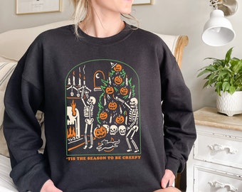 May include: Black sweatshirt with a graphic print of skeletons decorating a spooky Halloween tree with pumpkins and candles. The text "'Tis the season to be creepy" is printed below the graphic.