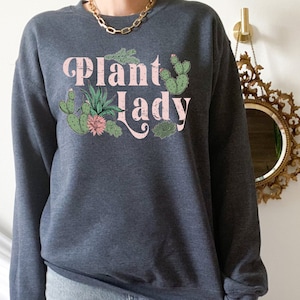 May include: A dark gray sweatshirt with the text "Plant Lady" in pink lettering and a graphic of cacti and succulents.