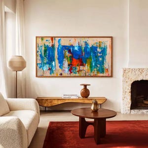 May include: An abstract painting with a wooden frame, featuring bold strokes of blue, orange, and green on a beige background. The room includes a wooden bench, a round coffee table, a red rug, and a cream-colored sofa. A floor lamp and decorative vases are also present.