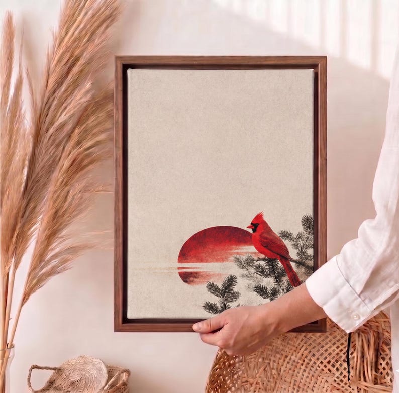 May include: A framed canvas art print featuring a red cardinal perched on a branch, set against a red sun and a neutral background. The artwork is encased in a dark wooden frame, creating a serene and natural aesthetic.