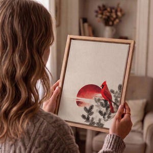 May include: A framed art print featuring a red cardinal perched on a branch, set against a red sun and a neutral background. The artwork is displayed in a light-colored wooden frame.