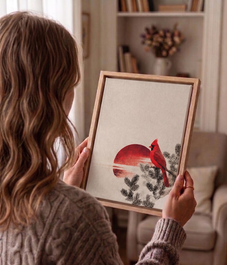 May include: A framed art print featuring a red cardinal perched on a branch, set against a red sun and a neutral background. The artwork is displayed in a light-colored wooden frame.
