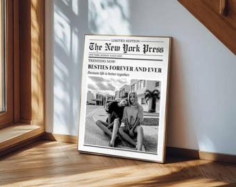 May include: A framed print of a newspaper page titled "The New York Press." The headline reads "BESTIES FOREVER AND EVER." The black and white image shows two people sitting together. The print is displayed on a wooden floor.