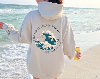 May include: Cream-colored hoodie with a circular graphic on the back featuring a stylized ocean wave in shades of blue and white. The text reads "WHEN YOU GO THROUGH DEEP WATERS, I WILL BE WITH YOU. ISAIAH 43:2."