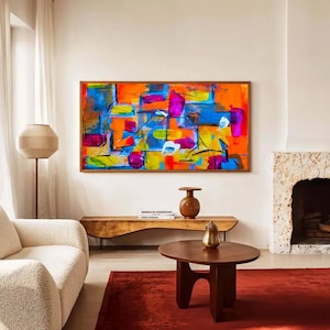 May include: Abstract art painting with a wooden frame. The artwork features a vibrant mix of colors, including orange, blue, pink, and yellow. The painting hangs above a wooden bench and a red rug. A round wooden coffee table and a white sofa are in the foreground.