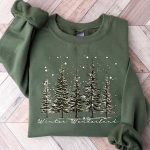 May include: A green sweatshirt with a winter wonderland design featuring a line of pine trees with snow falling around them. The text "Winter Wonderland" is printed below the trees.