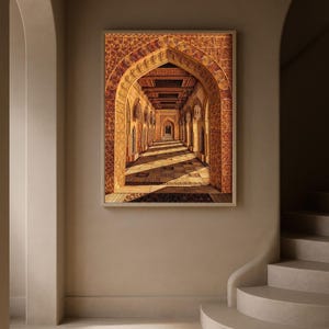 May include: A framed print of an arched hallway with intricate brickwork and a wooden ceiling. The perspective draws the eye down the corridor, with sunlight casting shadows on the floor. The artwork is displayed on a neutral-toned wall.