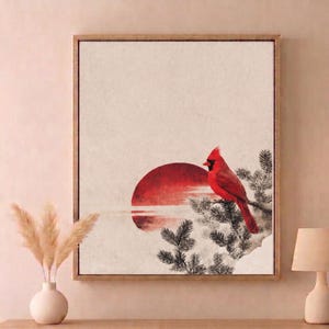 May include: Framed artwork featuring a vibrant red cardinal perched on a branch, set against a backdrop of a red sun and a neutral-toned sky. The artwork has a minimalist style with a wooden frame.